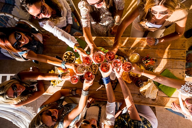 Gruppo di persone felici generazioni miste generazioni donne che si divertono tutti insieme durante la festa - vista verticale di demoni tintinnanti e brindando con vino rosso e tavolo pieno di cibo