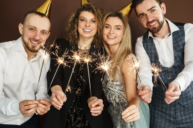 Foto gruppo di persone felici che indossano cappelli da festa con scintillii accesi durante le vacanze o la celebrazione di un evento