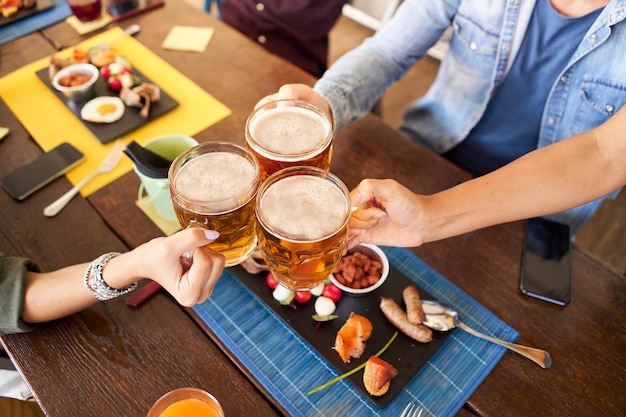 Un gruppo di amici felici e irriconoscibili che bevono e brindano alla birra al ristorante della birreria.