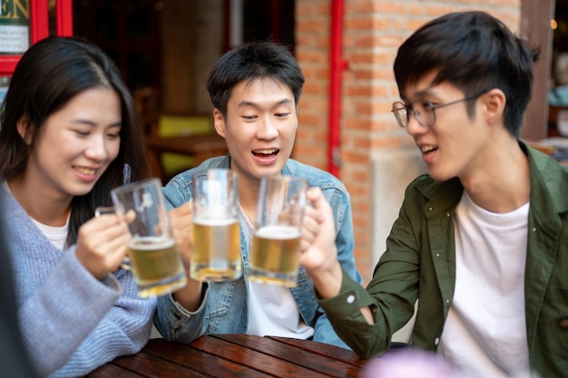 Photo group of happy young asian friends are enjoying drinking beers and talking at a bar together