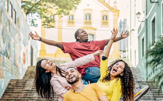 Group of happy young multiracial friends arms raised up having fun in the city street Friendship and travel concept Focus on the bearded man