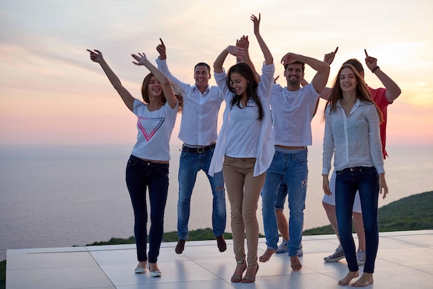 group of happy young people dancing and have fun on party in modern home bacony with sunset and ocean in background