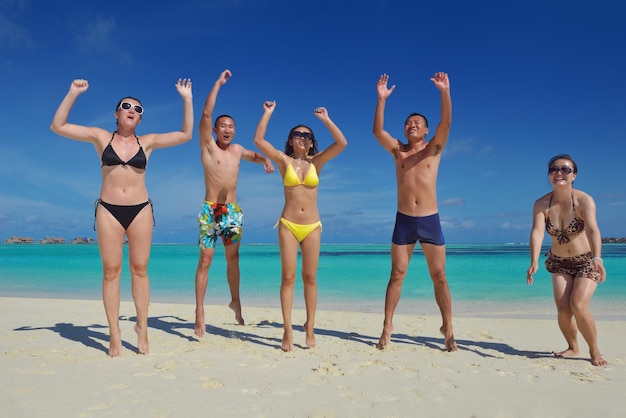 幸せな若者のグループは、美しい夏の日に白い砂浜で楽しんで喜びます