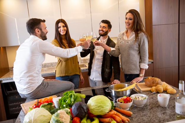 Group of happy young people preparing meal, drinking white wine and having a good time