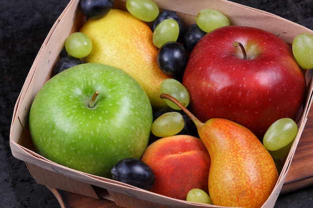 Group of healthy autumn colorful fruits on a dark background closeup Pears apples peach and grapes in a wooden basket on a wooden board