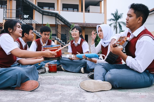 group of high school students sitting on the ground and playing musical instruments together