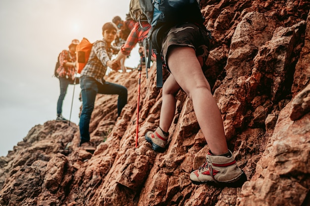 Gruppo di escursionisti che aiuta la sua amica a scalare l'ultima sezione del tramonto in montagna