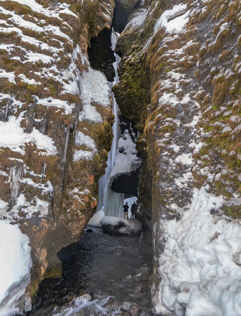 Photo group of hikers walking between the rocks of a frozen river being very careful not to fall and enter