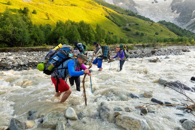 Group of hikers with backpack crossing a river on stones in Caucasian mountains Hiking and leisure theme Image with sunlight effect