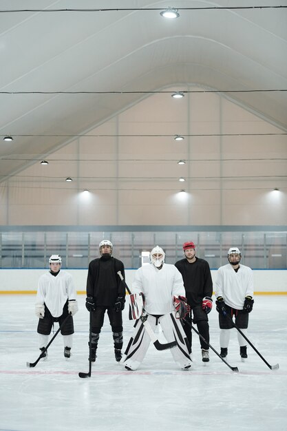 Gruppo di giocatori di hockey e il loro allenatore in uniforme sportiva, guanti, pattini e caschi protettivi in piedi sulla pista di pattinaggio in attesa di giocare