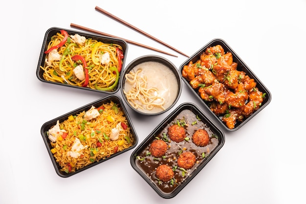 Group of home delivered Indo Chinese food in plastic packages, containers or boxes containing schezwan noodles, fried rice, chilli chicken, manchurian and soup.