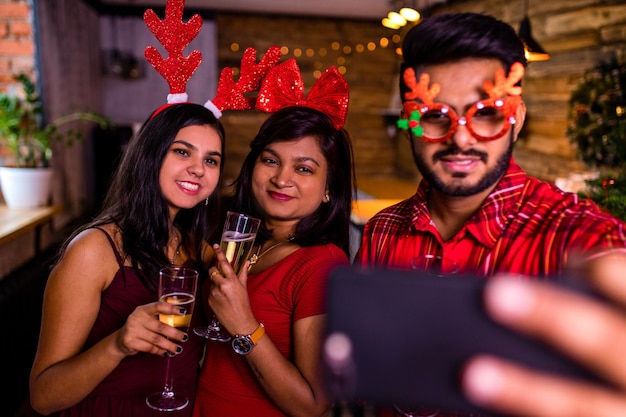 Group indian friends cheering with champagne flutes and making selfie photos on phone while having party on the kitchen at stay home quarantine corona virus outbreak party