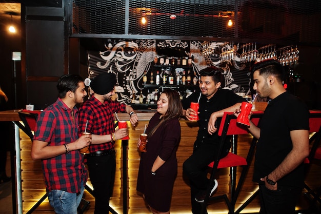 Group of indian friends having fun and rest at night club\
drinking cocktails near bar counter