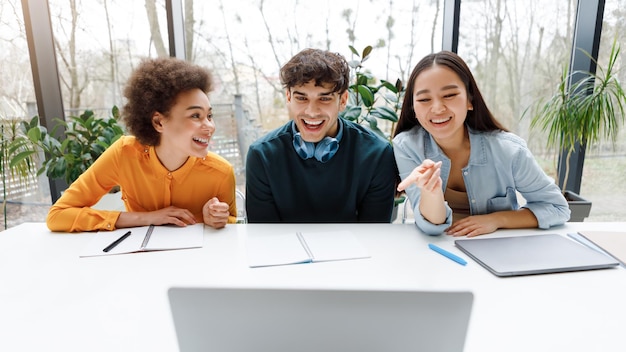 Group of international university students working with laptop ladies pointing at screen and smiling