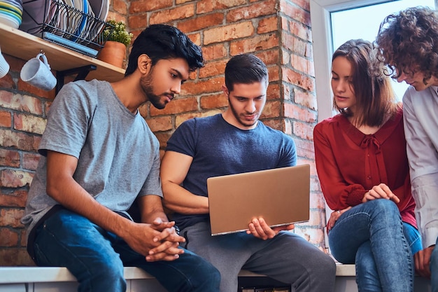 Group of interracial students with laptop and book doing lessons in a student dormitory.