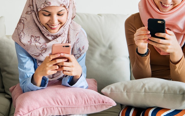 Photo group of islamic girls sitting on the couch and using smart phones