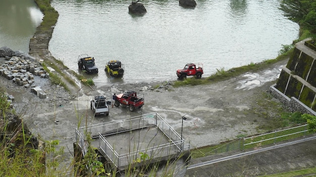 A group of jeeps are parked on the shore of a river.