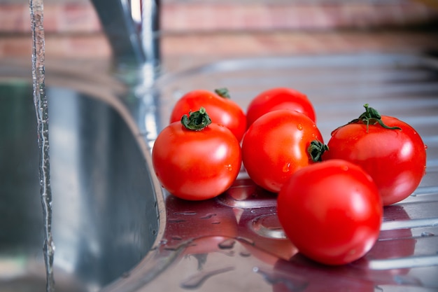 A group of juicy fresh red tomatoes in a queue for a wash. Wash fruits and vegetables before eating. Health and hygiene care.