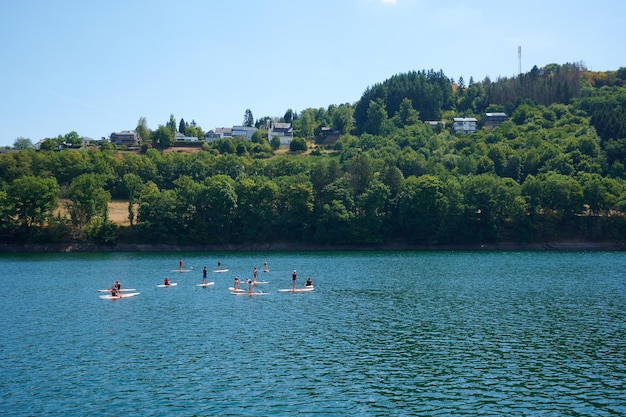 A group of kayaks in the blue lake with buildings on the lush green shore in the background