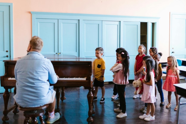 A Group of Kids Standing Near the Man Playing Piano Stock Photo