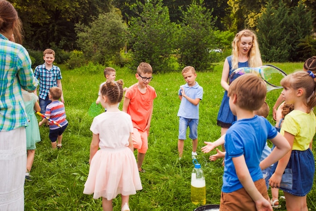 Group of kids with a caregiver make big soap bubbles in the garden