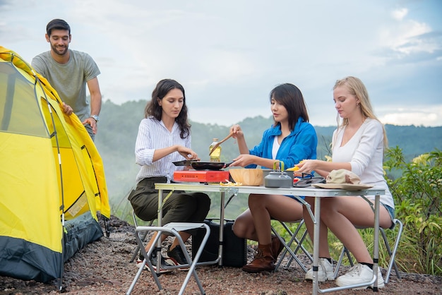 男性と女性の友人のグループは、美しい山々の真っ只中にピクニックテーブルと料理を設定します