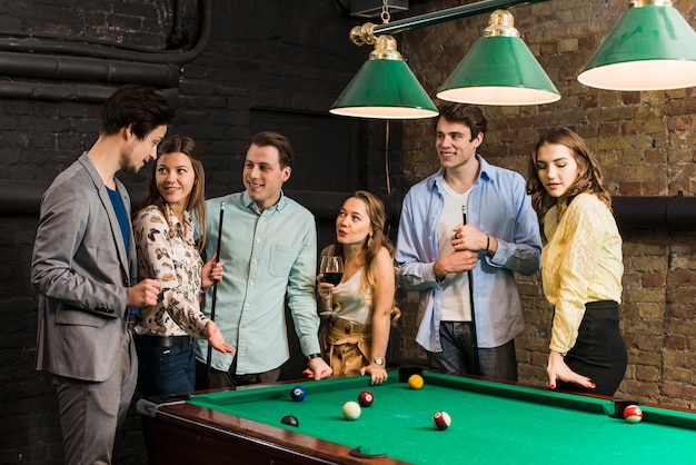 Group of male and female friends standing at pool table