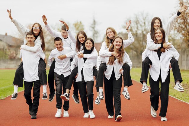 Foto un gruppo di molti adolescenti felici vestiti con lo stesso abito che si divertono e posano in uno stadio vicino a un college concetto di amicizia momenti di felicità amicizia scolastica