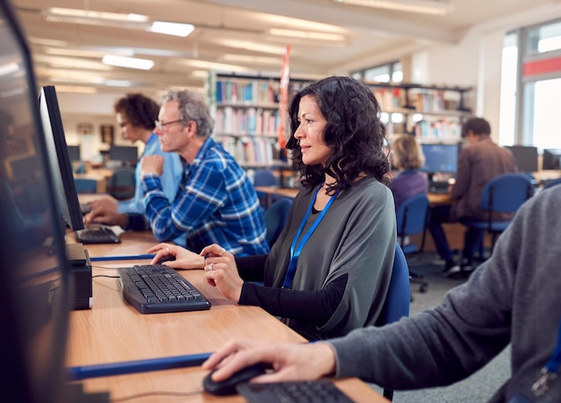 Group Of Mature Adult Students In Class Working At Computers In College Library