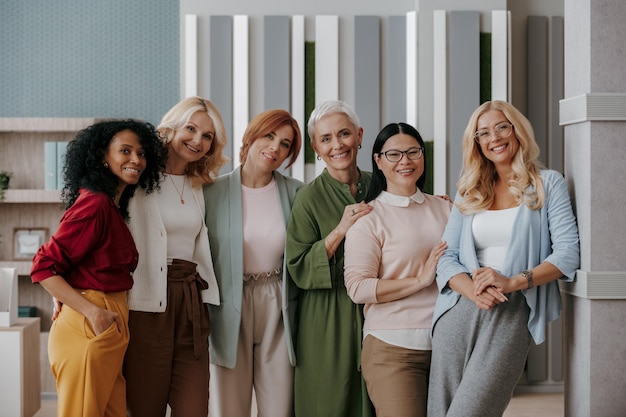 group of mature businesswomen bonding and smiling while standing in the office together