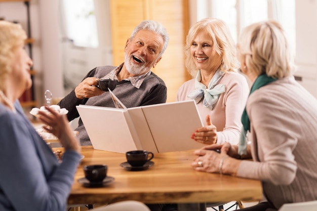 Group of mature friends talking and having fun while remembering their old times by looking at photo album at home