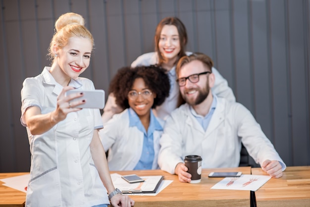 Photo group of medic students having fun photographing with phones during the coffee break at the classroom