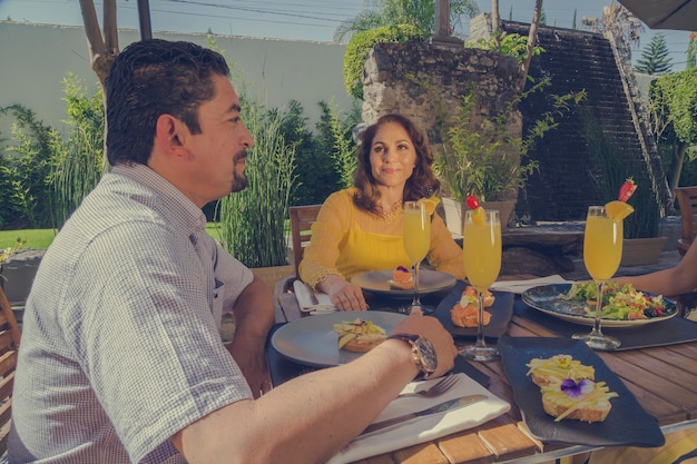 Group of middle-aged Latino friends enjoying food in the restaurant garden, salads and exotic drinks