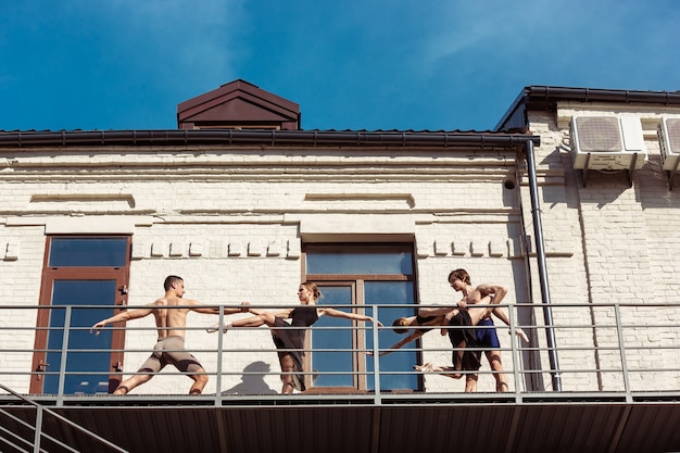 The group of modern ballet dancers performing on the stairs at the city. Fast moving of citylife, grace in daily things around. Graceful and flexible models in sunshine with buildings on background.