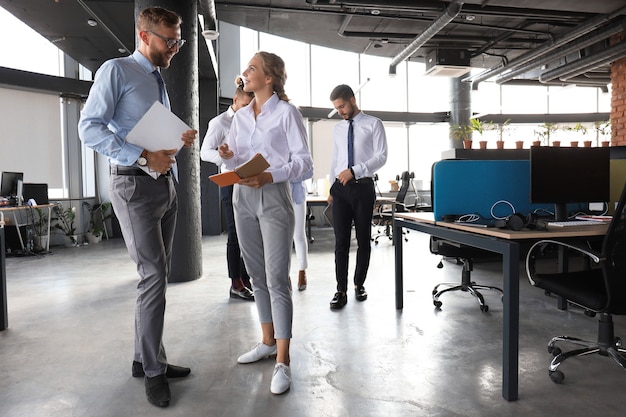 Group of modern business people are talking and smiling while standing in the office hallway.