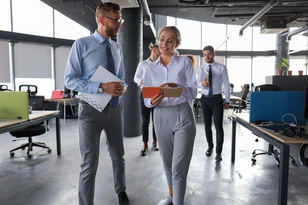 Group of modern business people are talking and smiling while standing in the office hallway.