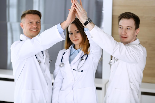 Group of modern doctors standing as a team while joining hands or giving five to each other