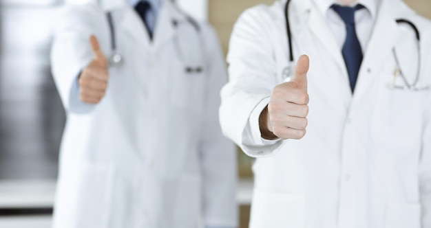 親指を立てるチームとして立っている現代の医師のグループ、または病院のオフィスのクローズアップでOKサインをしているヘルスケアと医学の概念における医療支援保険