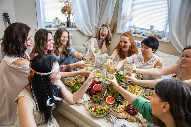 健康的な食事を提供するテーブルで休日を祝うグループの現代のヒッピーの女性の友人