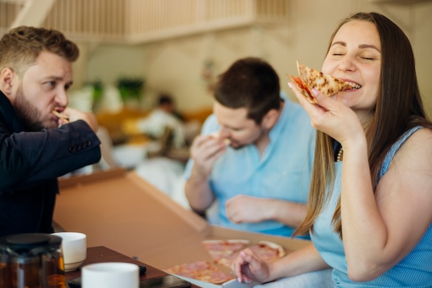 Group of modern people eating pizza sitting in cafeteria