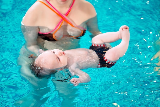 A group of mothers with their young children in a children's swimming class with a coach.