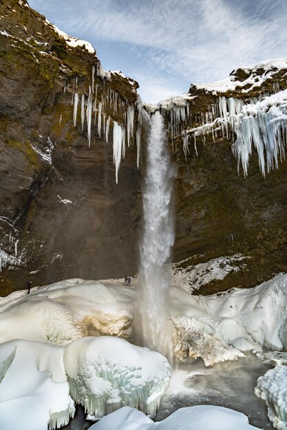 Group of mountaineering tourists behind the frozen Kvernufoss waterfall with snow and stalagmites