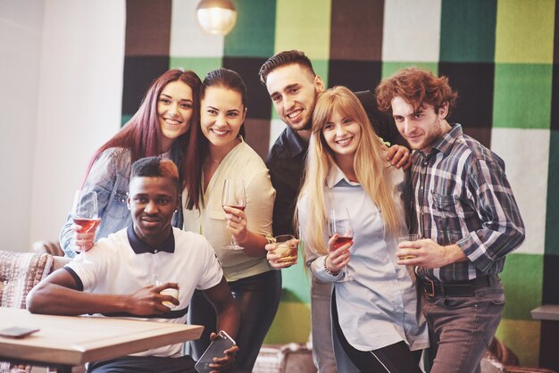 Group of multi-ethnic boys and girls with colorful fashionable clothes holding friend and posing on a green wall