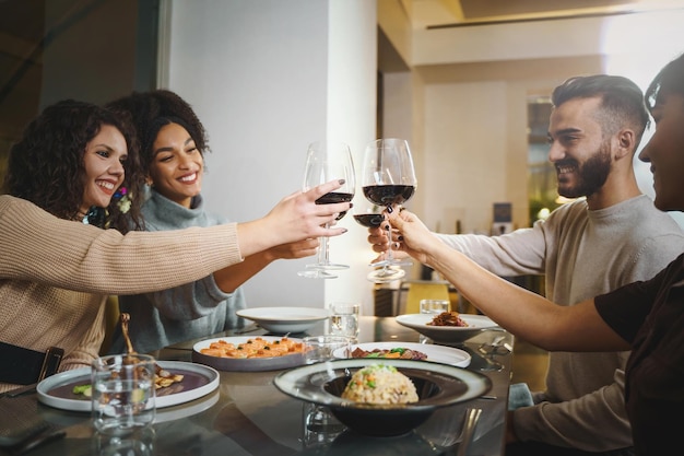 Photo group of multi-racial friends clinking wineglasses - gathering of friends toasting red wine at restaurant