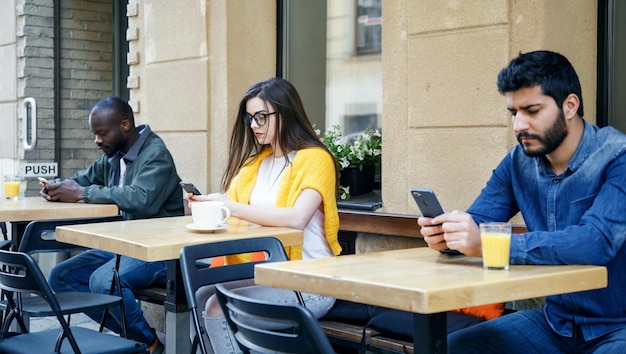 カフェに座ってスマートフォンで何かを入力している多文化の友人のグループ