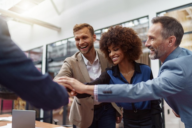 Group of multiethnic business people putting their hands together while standing in modern