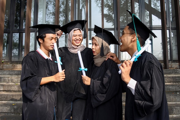 Group of multiethnic college students in mortar board and bachelor gowns with diplomas chatting and