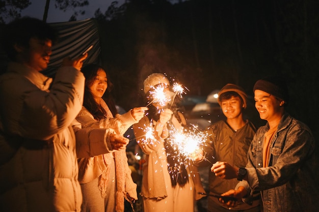 Group of multiethnic friends holding sparklers with happy expression young men and women enjoying o