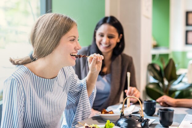 Group of multiethnic friends at restaurant having fun woman in foreground eating meat skewer