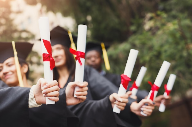 A group of multietnic students holding diplomas. Education, qualification and gown concept.